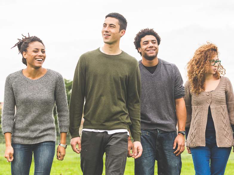 Pictured, a group of two young men and two young women walk under a grey sky with joyful expressions on their faces.