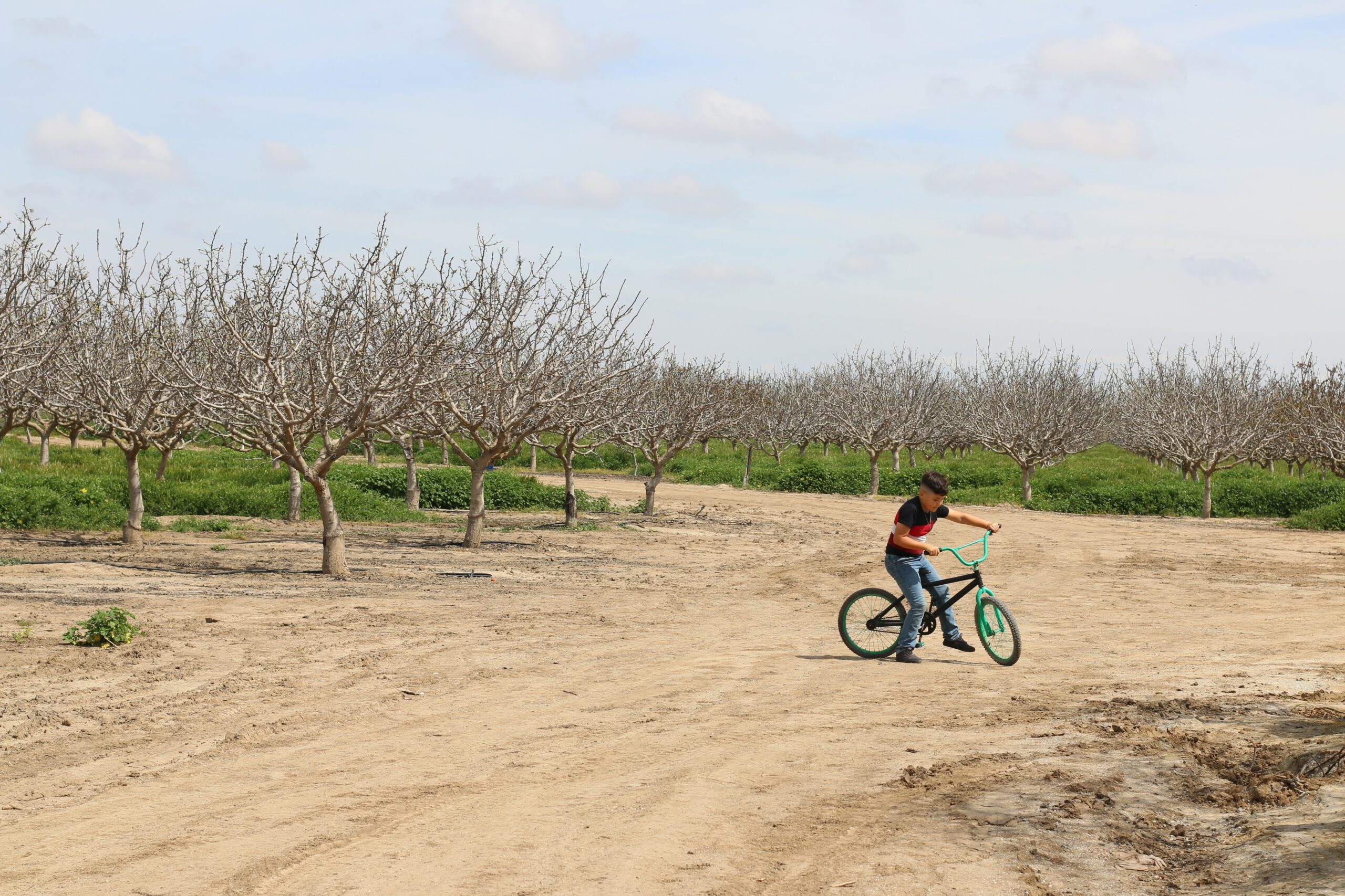 Pictured: A young child is pictured riding a bike through a dirt road in Arvin. Behind them, the sky is cloudy; there are small trees in the background.
