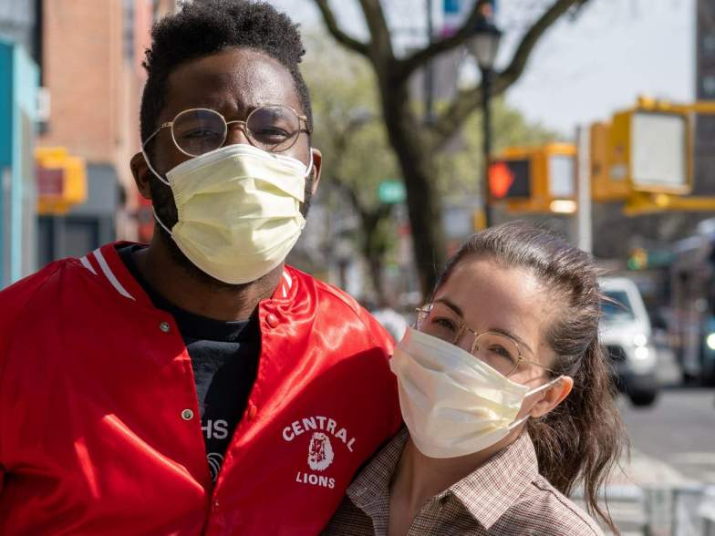 Pictured: Two people in masks pose for a photo on a sunny city street.